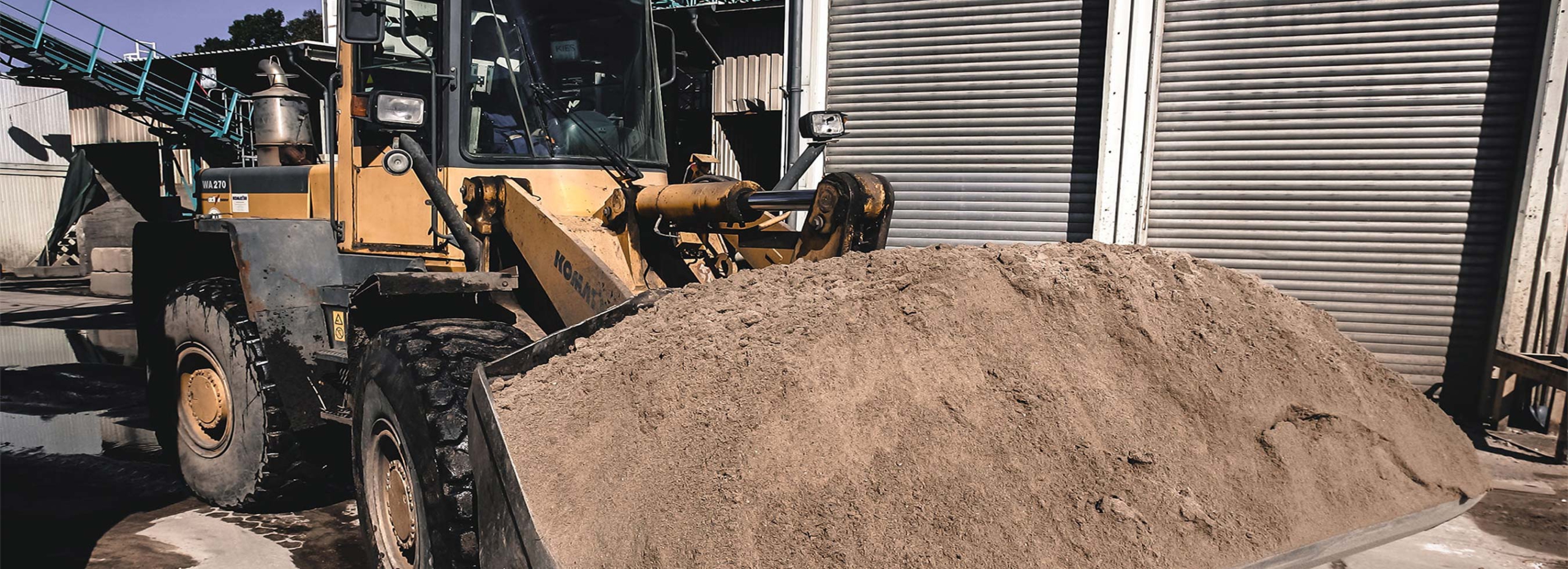 Bagger mit Sand auf der Schaufel fährt auf dem Gelände der GBAV Bodenwaschanlage